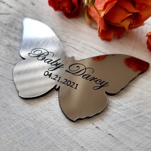 May include: A silver butterfly-shaped memorial ornament with the inscription "Baby Darcy 04.21.2021".