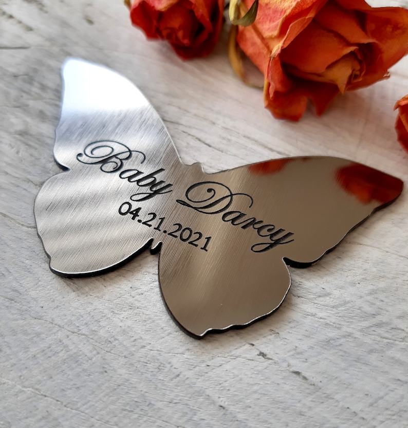 May include: A silver butterfly-shaped memorial ornament with the inscription "Baby Darcy 04.21.2021".