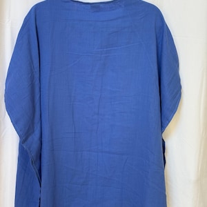 May include: A solid cornflower blue tunic top with a round neckline and short, wide sleeves. The garment features a loose, relaxed fit with side slits at the hem, constructed from a lightweight, opaque fabric that hangs straight down from the shoulders.