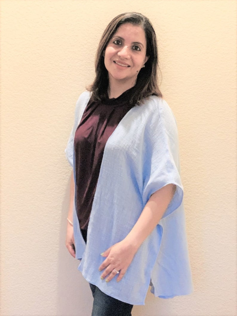May include: A light blue open-front kimono-style cardigan with short, wide sleeves and a textured fabric finish, layered over a dark maroon sleeveless top and dark blue denim jeans, creating a casual and layered outfit combination.
