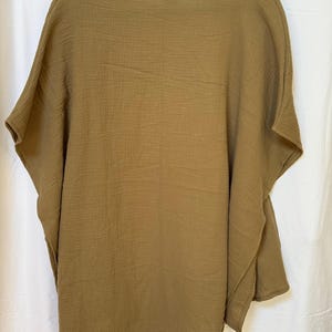 May include: A solid olive-brown poncho top featuring a wide, loose-fitting silhouette with short, integrated sleeves and a simple round neckline. The garment is crafted from a lightweight, textured fabric with a visible crinkled, gauze-like finish.