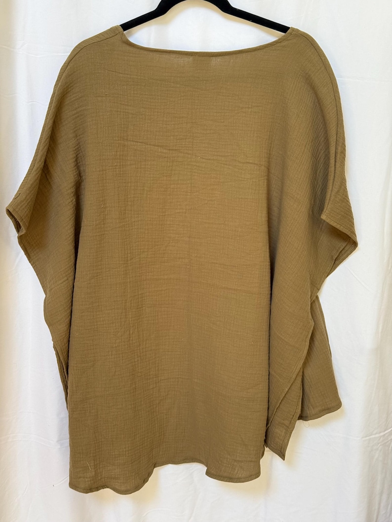 May include: A solid olive-brown poncho top featuring a wide, loose-fitting silhouette with short, integrated sleeves and a simple round neckline. The garment is crafted from a lightweight, textured fabric with a visible crinkled, gauze-like finish.