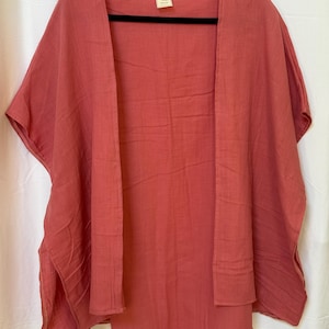 May include: A solid dusty rose colored open-front kimono style garment with short sleeves and side slits. The fabric has a visible crinkled texture. A small rectangular label with the text Malf is attached to the inside of the neckline.