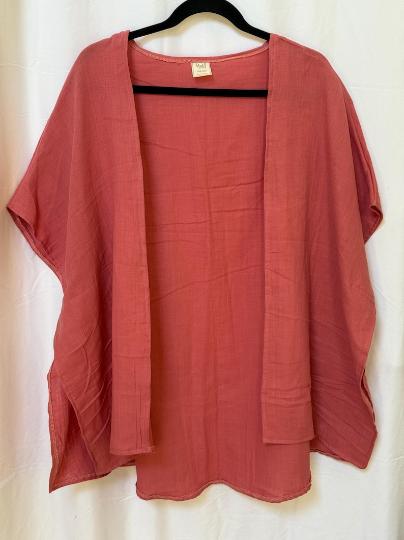 May include: A solid dusty rose colored open-front kimono style garment with short sleeves and side slits. The fabric has a visible crinkled texture. A small rectangular label with the text Malf is attached to the inside of the neckline.