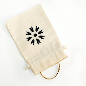 May include: A small, white cotton drawstring bag with a black floral design. The bag is tied with a string and contains a gold bracelet.