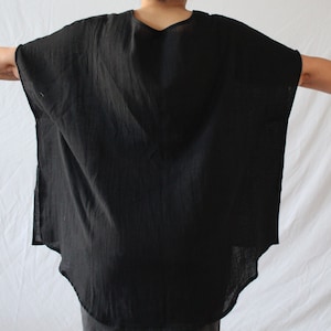 May include: A solid black, loose-fitting tunic top with a wide, boxy silhouette and short, integrated sleeves. The garment features a rounded neckline and a curved hemline that is slightly longer in the back, crafted from a lightweight fabric.
