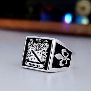Puede incluir: Un anillo de sello de plata con un escudo de esmalte negro que presenta un escudo de armas y el nombre "Howard".