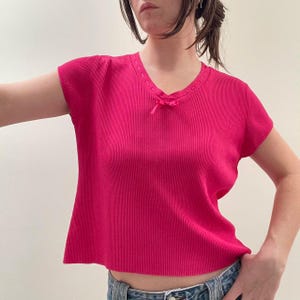 May include: A bright pink ribbed knit top with short sleeves and a small bow at the neckline.
