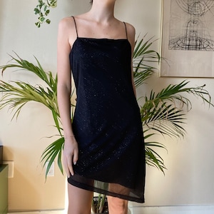 May include: A black spaghetti strap dress with a sparkly texture and a sheer overlay at the bottom.