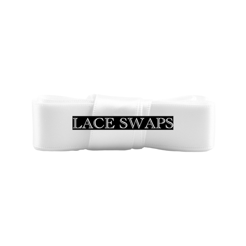 May include: A roll of smooth white satin ribbon featuring a black rectangular label centered on the front. The label contains the white text LACE SWAPS in a serif font. The ribbon is tightly wound and has a consistent, clean appearance.