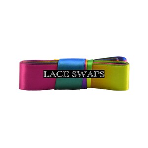May include: A folded length of multi-colored satin ribbon featuring a smooth, reflective texture. The ribbon displays a gradient of vibrant colors including pink, blue, green, and yellow. The text LACE SWAPS is printed in white on a black bar.