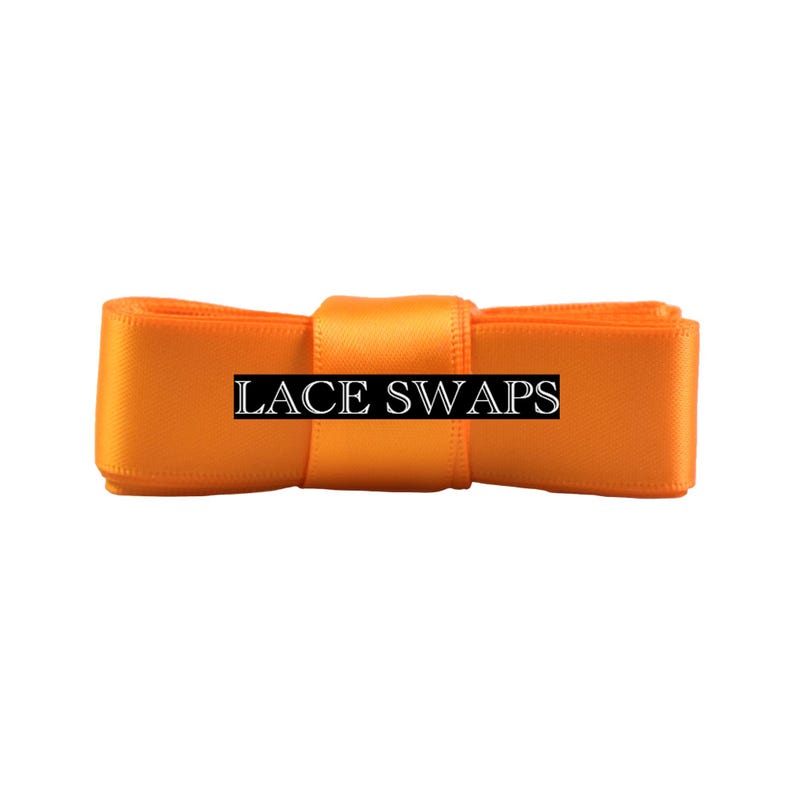 May include: A bright orange satin ribbon folded into a rectangular shape with a central band. The text LACE SWAPS is printed in a white serif font on a black rectangular background centered across the front of the orange ribbon.