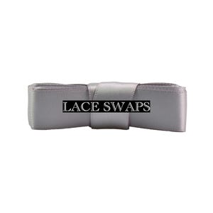 May include: A light gray satin ribbon folded into a rectangular shape with a central band. The text LACE SWAPS is printed in white capital letters on a black rectangular background centered across the front of the smooth, reflective fabric.