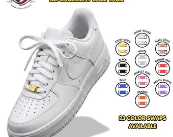 May include: A white low-top sneaker featuring a gold AF1 dubrae lace tag. The image displays text reading AF1 DUBRAES REPLACEMENT LACE TAGS and 23 COLOR SWAPS AVAILABLE, alongside a color chart showing options in shiny gold, silver, rose gold, white, black, red, pink, blue, purple, and orange.