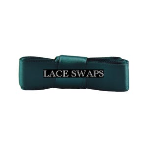 May include: A dark emerald green satin ribbon folded into a rectangular shape with a central band. The text LACE SWAPS is printed in white capital letters across the center of the ribbon, which features a smooth, reflective fabric texture.