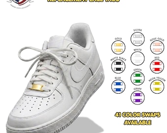 May include: A white sneaker featuring a gold metal lace tag on the laces. The image displays text reading METAL LACE TAG 1.25 REPLACEMENT LACE TAGS and 41 COLOR SWAPS AVAILABLE, alongside a color chart showing silver, gold, rose gold, white, matte black, red, blue, green, neon yellow, and grape tags.