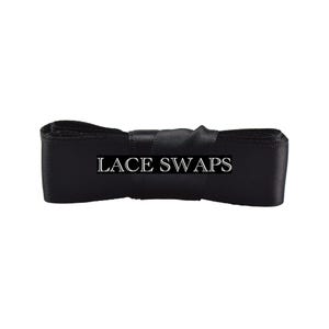 May include: A roll of black satin ribbon featuring a smooth, reflective texture. The text LACE SWAPS is printed in white capital letters across the center of the ribbon, which is neatly coiled and secured in a horizontal orientation.