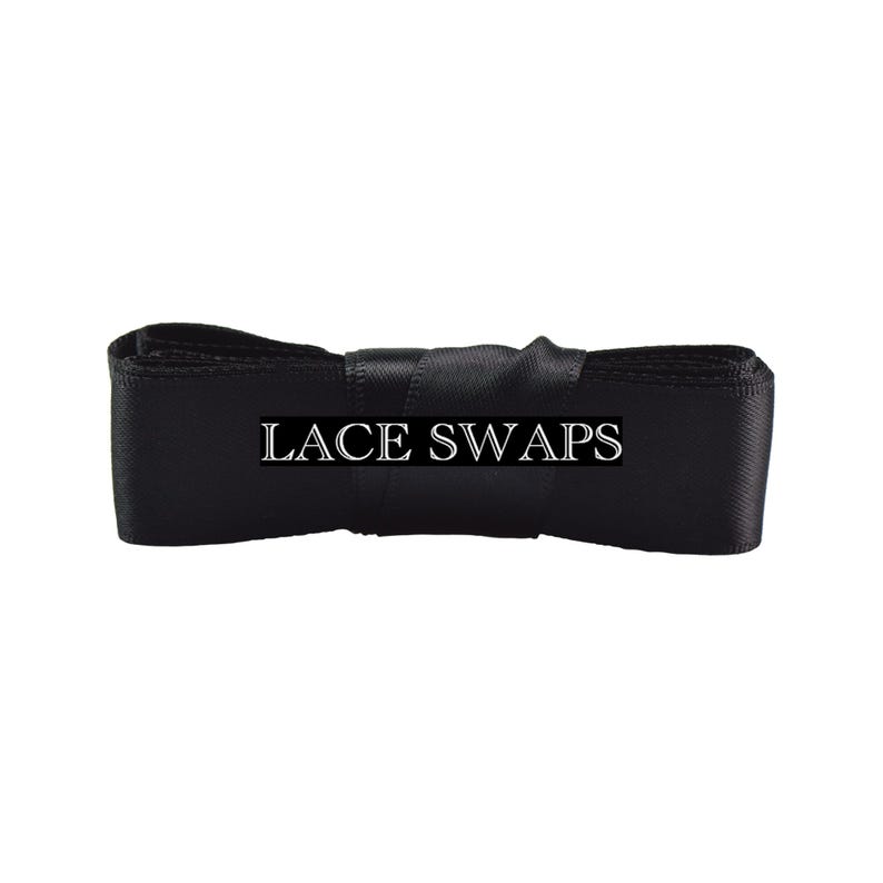 May include: A roll of black satin ribbon featuring a smooth, reflective texture. The text LACE SWAPS is printed in white capital letters across the center of the ribbon, which is neatly coiled and secured in a horizontal orientation.