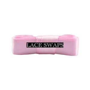 May include: A roll of light pink satin ribbon with a smooth, reflective texture. The ribbon is wound into a compact, cylindrical shape. A black rectangular label with the white text LACE SWAPS is centered across the front of the ribbon.