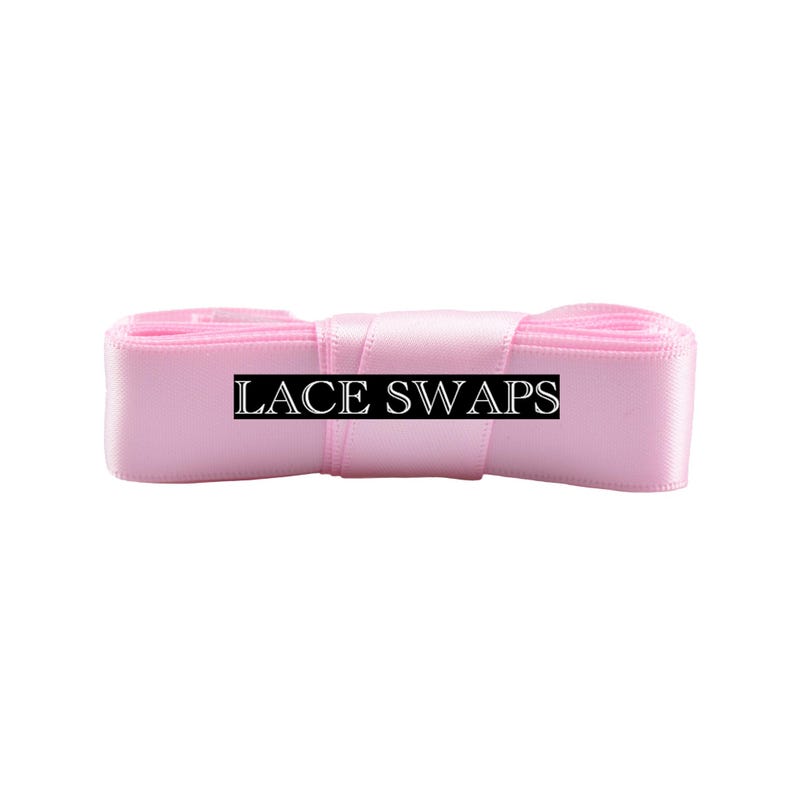 May include: A roll of light pink satin ribbon with a smooth, reflective texture. The ribbon is wound into a compact, cylindrical shape. A black rectangular label with the white text LACE SWAPS is centered across the front of the ribbon.