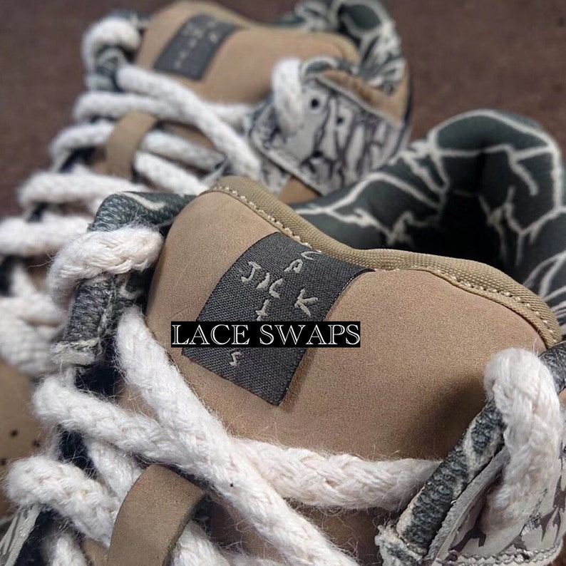 May include: Close-up of a pair of tan sneakers with a camouflage pattern and white laces. The text "LACE SWAPS" is printed on the tongue of the shoe.