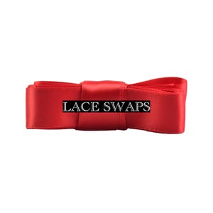 May include: A bright red satin ribbon folded into a bow shape with a smooth, reflective texture. The text LACE SWAPS is printed in a white serif font across the center of the ribbon, which is horizontally oriented against a plain background.