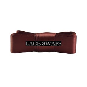 May include: A dark burgundy satin ribbon folded into a rectangular shape with a smooth, reflective finish. The text LACE SWAPS is printed in white capital letters across the center of the ribbon, which is secured by a central band of fabric.