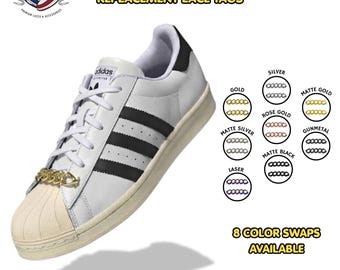 May include: A white sneaker with black stripes and a gold-colored Cuban link lace tag. Text reads: CUBAN LINK DUBRAE REPLACEMENT LACE TAGS. Eight color options are displayed: gold, silver, matte gold, rose gold, matte silver, gunmetal, laser, and matte black.