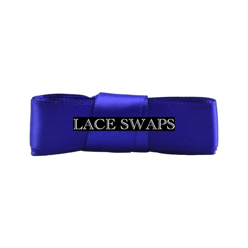 May include: A vibrant royal blue satin ribbon folded into a rectangular shape, featuring the text LACE SWAPS printed in a white serif font across the center. The smooth, reflective fabric has a distinct sheen and a consistent, deep blue color.