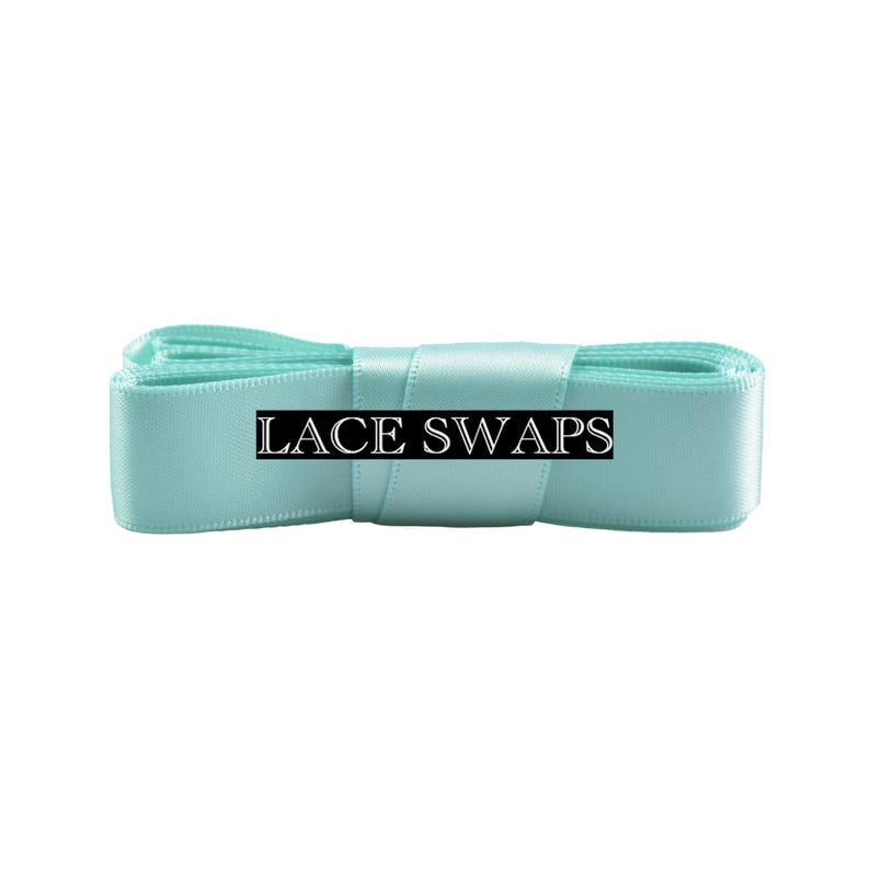 May include: A folded length of smooth, light turquoise satin ribbon with a subtle sheen. A black rectangular label is centered on the ribbon, featuring the white text LACE SWAPS in a serif font. The ribbon is neatly coiled and horizontally oriented.