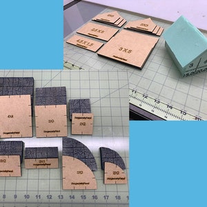 Puede incluir: Un conjunto de piezas de madera y espuma para crear edificios en miniatura y baldosas de mazmorra. Las piezas están etiquetadas con medidas en pulgadas, como 4x4, 3x3 y 2x2. La pieza de espuma es de color verde claro y tiene forma de techo.