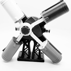 May include: A 3D-printed model of a mechanical device, featuring a central black hub with four cylindrical components in white, gray, and black. The model is supported by a black base with a lattice structure.