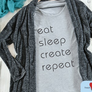 May include: A gray t-shirt with the text "eat sleep create repeat" printed in black.
