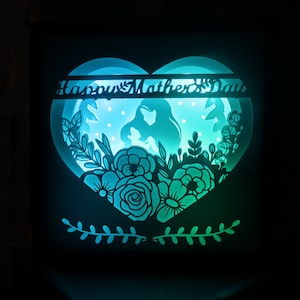 May include: A teal and blue illuminated papercraft heart with a floral design and the text "Happy Mother's Day".