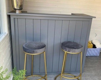 May include: Two gold bar stools with gray velvet seats. The stools are in front of a gray wooden bar counter.