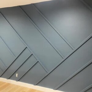 Op de afbeelding: Een muur met een geometrisch patroon gemaakt van geschilderde houten panelen. De panelen zijn in een diagonaal patroon gerangschikt en in een lichtblauwe kleur geverfd.