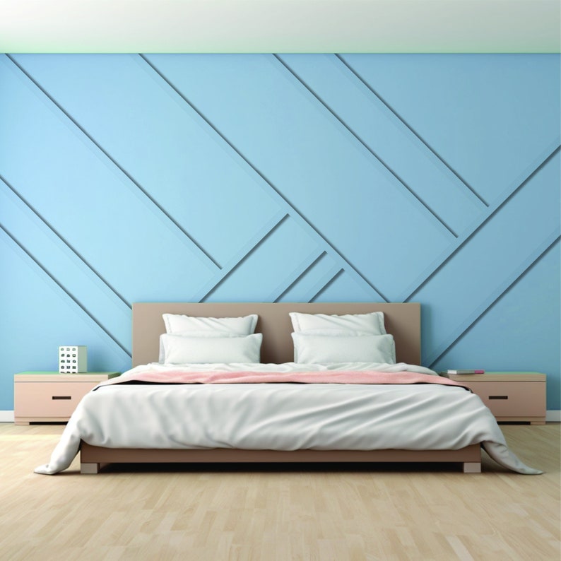 Op de afbeelding: Een wit bed met een lichtbruine hoofdeinde en een lichtroze deken. Het bed staat in een kamer met een lichtblauwe muur met een geometrisch patroon.