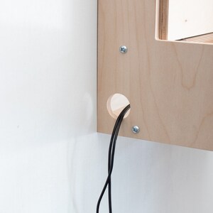 May include: A close-up of a wooden shelf with a hole for cords. Two black cords are coming out of the hole.