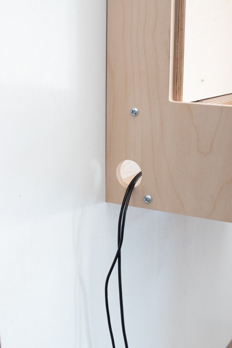 May include: A close-up of a wooden shelf with a hole for cords. Two black cords are coming out of the hole.