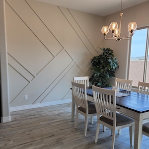 Pode incluir: Uma sala de jantar com uma mesa de madeira escura e cadeiras com pernas brancas e almofadas cinzentas. A sala tem uma parede decorativa com pain&eacute;is geom&eacute;tricos e um candelabro com luzes em forma de globo. O ch&atilde;o &eacute; de madeira clara.