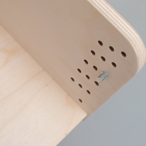 May include: Close-up of a light wood shelf with a silver metal screw. The shelf has a pattern of evenly spaced holes.