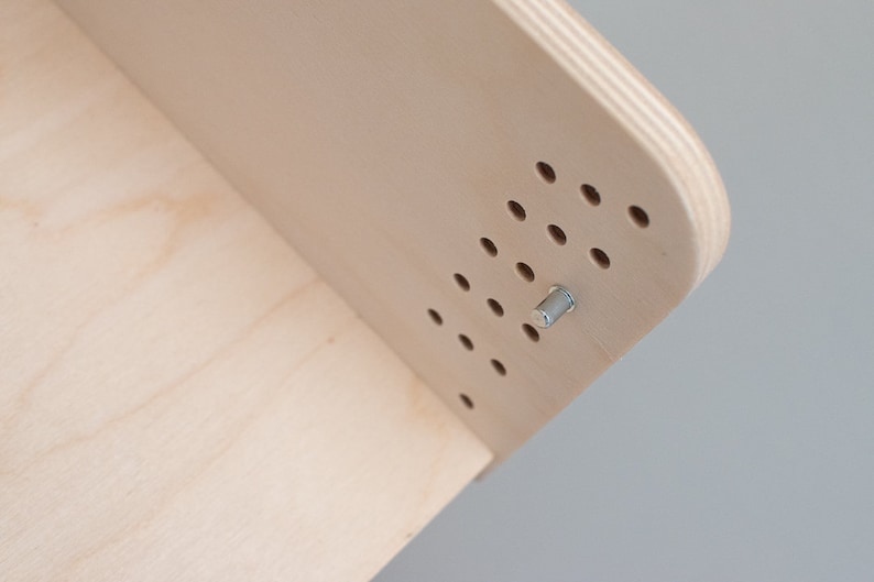 May include: Close-up of a light wood shelf with a silver metal screw. The shelf has a pattern of evenly spaced holes.