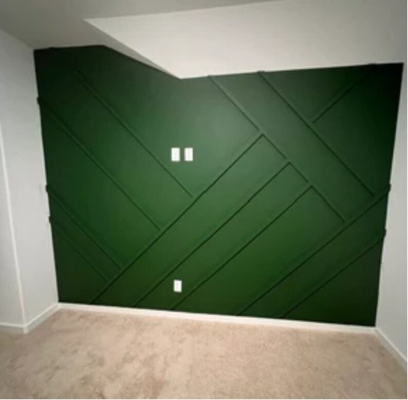 Op de afbeelding: Een groene accentmuur met een geometrisch patroon. De muur is in een diep groen geverfd en heeft een reeks verhoogde panelen die een ruitpatroon cre&euml;ren. Er zijn twee witte stopcontacten op de muur.