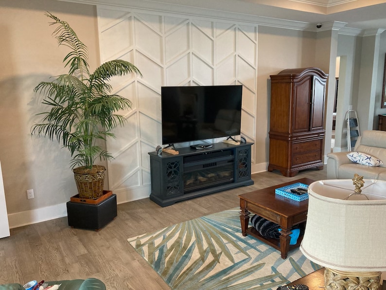 Pode incluir: Uma sala de estar com uma grande TV de tela plana acima de uma lareira. Um arm&aacute;rio alto de madeira escura est&aacute; &agrave; direita. Uma grande palmeira em vaso est&aacute; &agrave; esquerda, e um tapete estampado est&aacute; no ch&atilde;o.