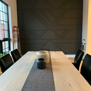 Pode incluir: Uma sala de jantar com uma grande mesa de madeira clara, com um corredor cinza e cadeiras pretas. Vasos decorativos est&atilde;o sobre a mesa. A parede de destaque cinza escuro apresenta um design geom&eacute;trico.