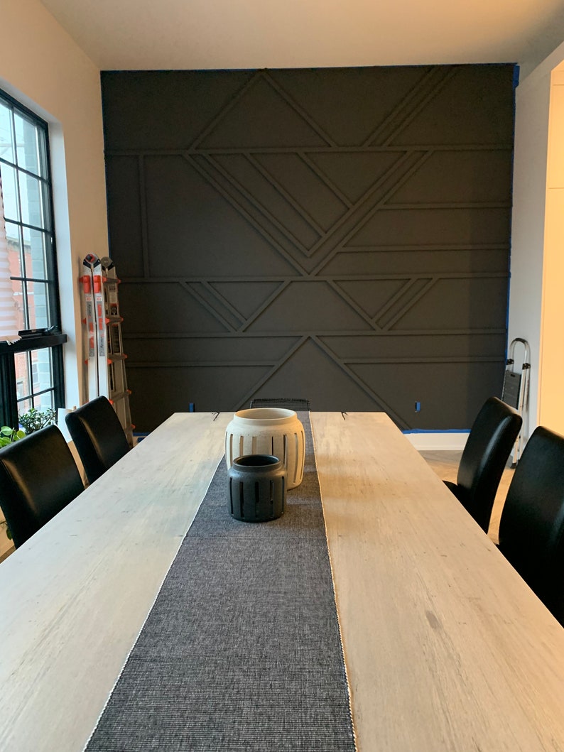 Pode incluir: Uma sala de jantar com uma grande mesa de madeira clara, com um corredor cinza e cadeiras pretas. Vasos decorativos est&atilde;o sobre a mesa. A parede de destaque cinza escuro apresenta um design geom&eacute;trico.