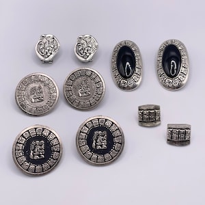 May include: A set of silver and black earrings and buttons with intricate designs. The earrings are oval shaped with black centers and the buttons are round with a raised design.
