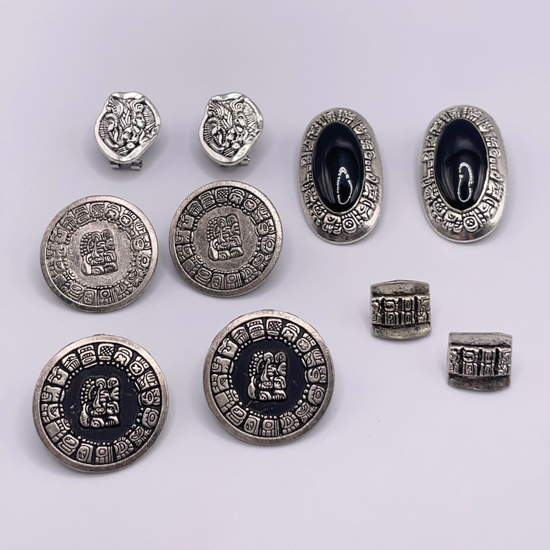 May include: A set of silver and black earrings and buttons with intricate designs. The earrings are oval shaped with black centers and the buttons are round with a raised design.