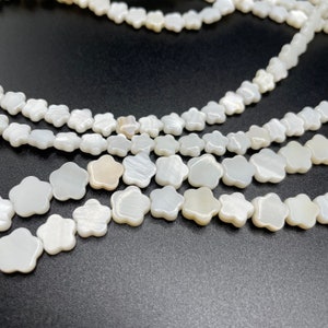 Op de afbeelding: Een streng witte schelpbloem kralen. De kralen zijn gerangschikt in een bloemvorm en zijn geregen op een wit koord.