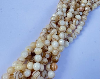 May include: Strands of cream-colored beads with brown and tan stripes. The beads are round and appear to be made of a natural material. The beads are strung together, creating a flowing, organic look. The beads are a neutral color, suitable for jewelry making.